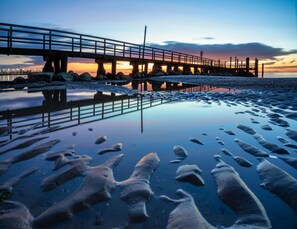 A pier extending over calm waters with a sunset in the background. - Ferienwohnung, Wyk auf Fohr (Wyk auf Foehr)