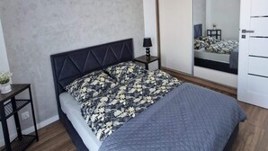 A modern bedroom with a bed, a nightstand, a lamp, a mirror, and a wardrobe. - Comfortable Holiday Apartment Close to the sea (Mielno)