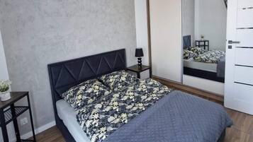 Ein modernes Schlafzimmer mit Bett, Nachttisch, Lampe, Spiegel und Kleiderschrank.
