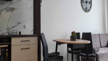 Eine moderne Küche mit Marmor-Spritzschutz, einem eingebauten Backofen und einem Essbereich mit rundem Tisch und vier Stühlen. Über dem Esstisch ist eine Wanduhr zu sehen.