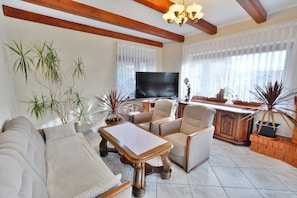 Una sala de estar con sofá, sillones, una mesa de centro, televisor y plantas en macetas.