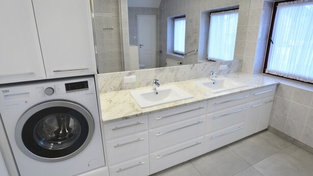 Een moderne badkamer met een wasmachine, twee wastafels, een grote spiegel en een raam met gordijnen.