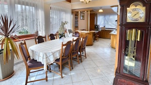 Un coin repas avec une table et des chaises en bois, une grande horloge et une cuisine en arrière-plan.