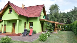 Una casa a due piani con tetto in tegole rosse, pareti esterne verdi e un piccolo balcone con un'altalena in legno.