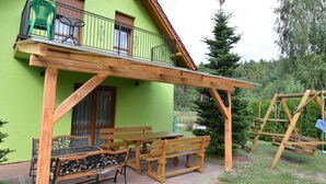 Una casa verde con un balcone, panche in legno, tavoli da picnic e un’altalena.