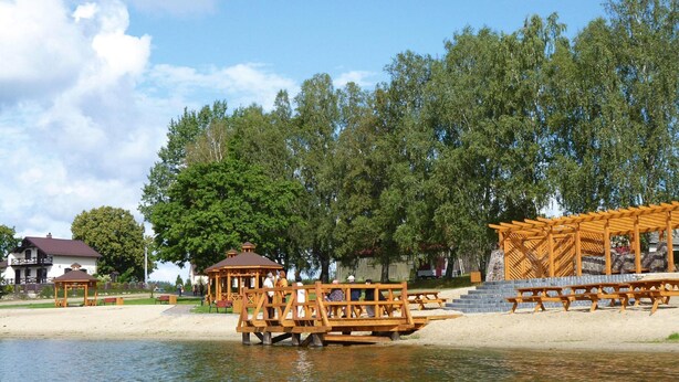 Una terrazza in legno sul lago con tavoli da picnic e gazebo.