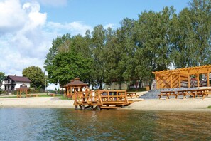A lakeside wooden deck with picnic tables and gazebos. - Holiday Home in Bytow Near Sandy Lake Beach (Lipnica)