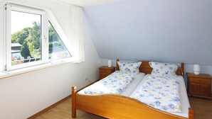 Une chambre à coucher avec un lit en bois, deux tables de chevet, une fenêtre avec des rideaux et une vue sur la verdure.