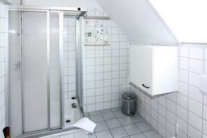 A small, tiled bathroom with a shower, a waste bin, and a white cabinet. - Ferienanlage Schuldt, Behrensdorf (Behrensdorf)