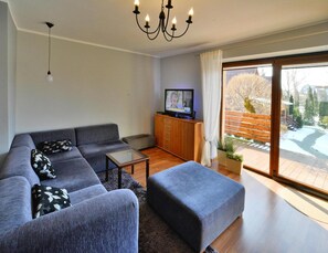 A modern living room with a sectional sofa, a glass coffee table, a television, and a sliding glass door leading to a deck. - Comfortable Holiday Home With a Garden, Kolobrzeg (Kołobrzeg)