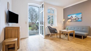 Ein modernes Wohnzimmer mit Holzboden, grauem Sofa, Holztisch, grauem Sessel und Fernseher auf einer Holzkommode.
