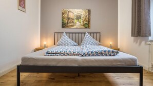 Ein Schlafzimmer mit einem Bett, zwei Nachttischen, einem Bild an der Wand und einem Fenster mit Vorhängen.