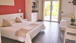 A hotel room with a bed, a desk, a kitchenette, and a sliding glass door to the outside. - Village Mobile Home in Rebi (Imperia)