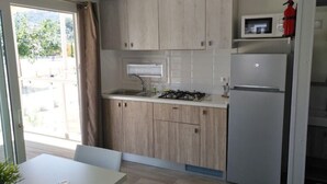 A compact kitchen with light wood cabinets, a gas stove, a microwave, and a refrigerator. - Village Mobile Home in Rebi (Imperia)