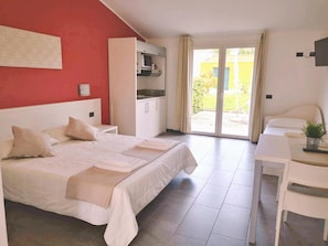 A hotel room with a bed, a desk, a kitchenette, and a sliding glass door to the outside. - Village Mobile Home in Rebi (Imperia)