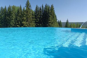 A clear blue swimming pool surrounded by dense green trees.