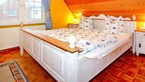 A bedroom with a wooden ceiling, a bed with a white headboard, a nightstand with a lamp, and a window with curtains.