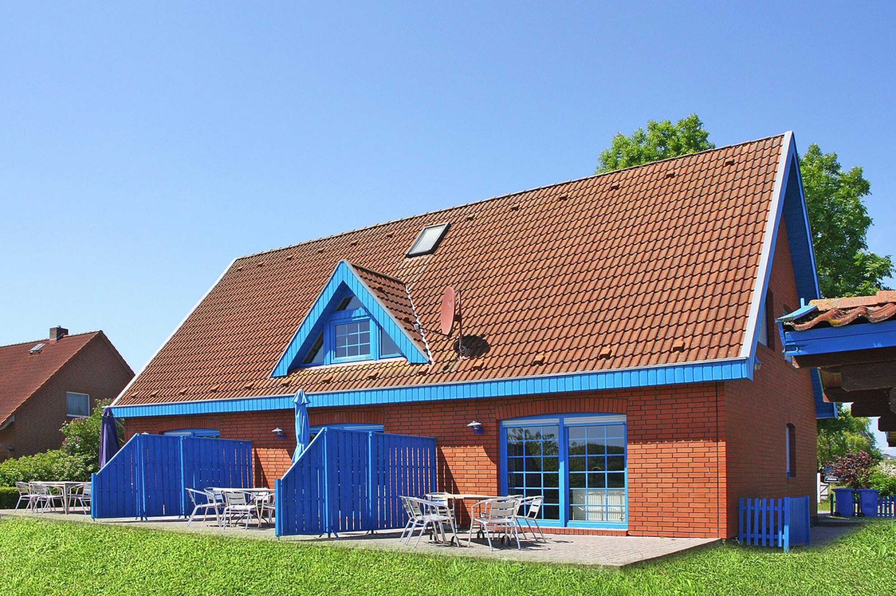 Il s’agit d’un bâtiment à deux étages, construit en briques, avec un toit en pente, des éléments décoratifs bleus et une petite fenêtre de toit. On y trouve des tables et des chaises à l’extérieur, ainsi qu’une clôture bleue qui entoure la propriété.