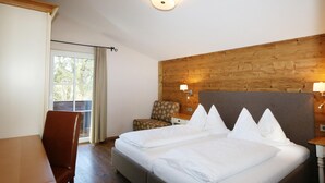 A hotel room with a bed, a chair, a desk, a wooden wall, and a window with curtains.