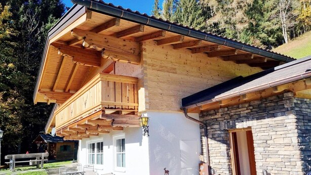 A wooden chalet with a balcony, stone exterior, and outdoor seating area.