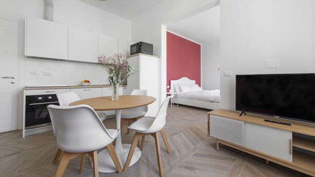 Een moderne keuken met witte kasten, een inbouwoven en een eethoek met een ronde tafel en stoelen.