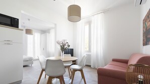Ein modernes, helles Wohnzimmer mit Esstisch, Stühlen, einer Couch und einer Zimmerpflanze.