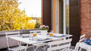 Ein Balkon mit Tisch für zwei Personen, einem Blumentopf und einer Tür mit Fensterläden.