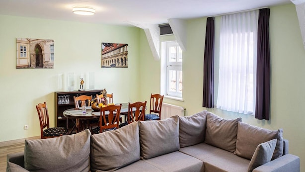 A living room with a sectional sofa, a dining table with chairs, and two paintings on the wall. - Ferienwohnung Schlossblick, Wernigerode (Wernigerode)