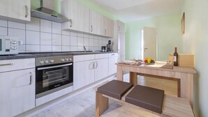 A modern kitchen with white cabinets, a built-in oven, and a wooden dining table with benches. - Ferienwohnung Schlossblick, Wernigerode (Wernigerode)