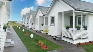 En rad vita, flyttbara hus med grå tak, där varje hus har en veranda och krukväxter.