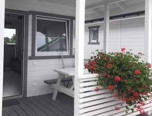 A covered porch with a bench and a potted plant with red flowers. - Single-story Holiday Homes With Terraces (Mielno)