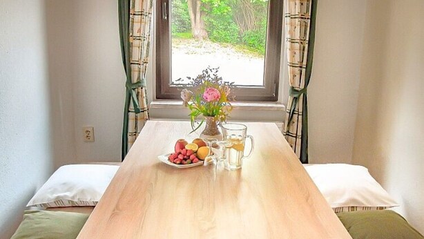 Ett träbord med en vas med blommor, en tallrik med frukt och två glas vatten.