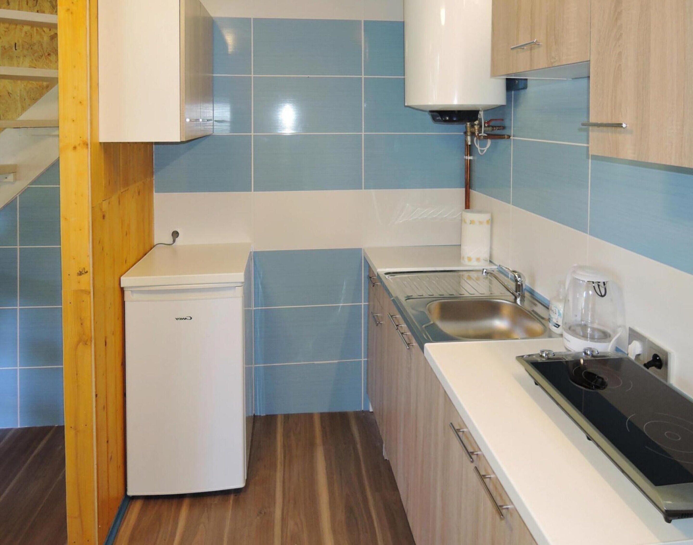 A compact kitchen with blue and white tiles, a small refrigerator, a sink, and a stove.