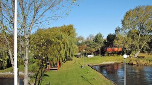 A flagpole with the European Union flag, a weeping willow tree, a small wooden bench, and a pond in a park setting. - Holiday Home in Sulomino With Private Beach (gmina Wolin)
