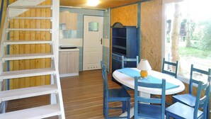 A room with a wooden floor, a white ladder, a table with blue chairs, and a window with a view of trees. - Holiday Home in Sulomino With Private Beach (gmina Wolin)
