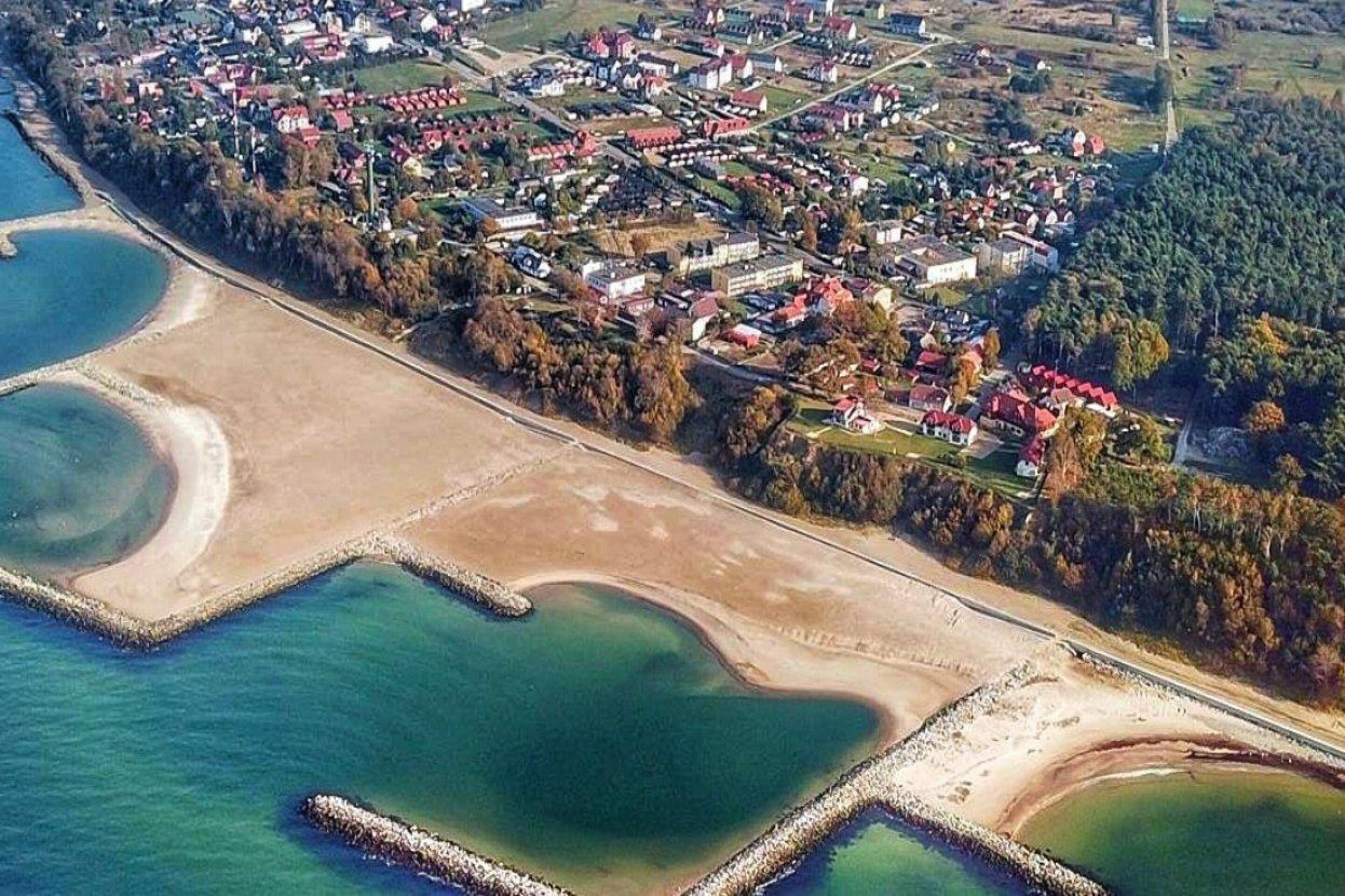 Vista aerea di una località costiera con zone residenziali, una spiaggia e un’ampia distesa d’acqua.
