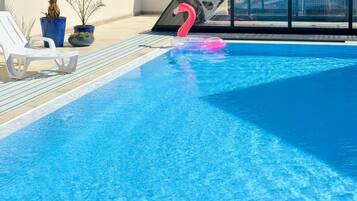 A swimming pool with a pink flamingo float, white lounge chairs, and potted plants.
