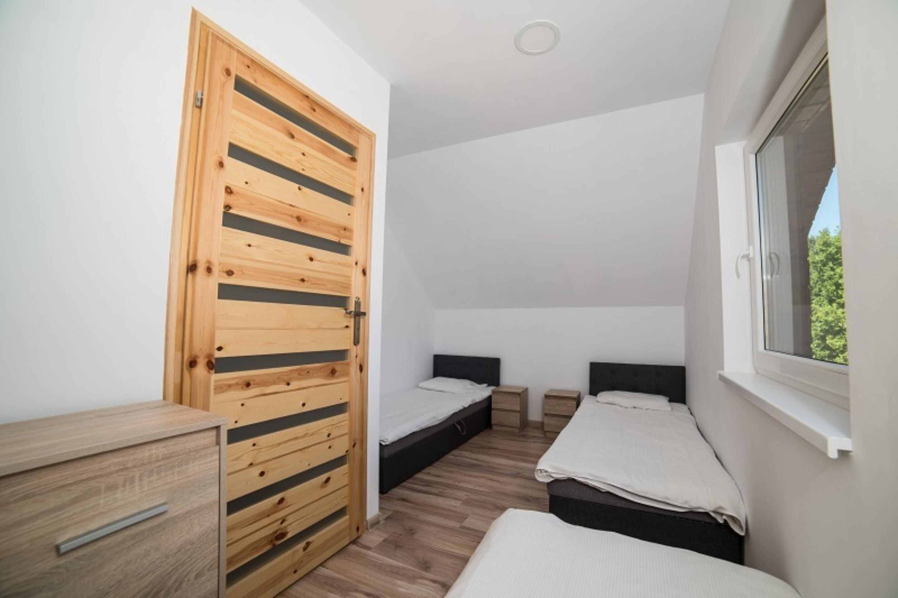 A bedroom with two beds, a wooden wardrobe, and a window.