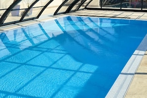 A clear blue swimming pool with a tiled edge and a glass enclosure on one side.