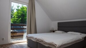 Une chambre dotée d’un grand lit, d’une table de chevet, d’une fenêtre donnant sur un paysage verdoyant et d’un balcon avec une balustrade.
