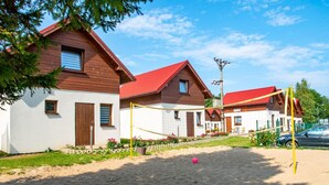 Une rangée de maisons en bois aux toits rouges, un filet de volley-ball et une zone sablonneuse.