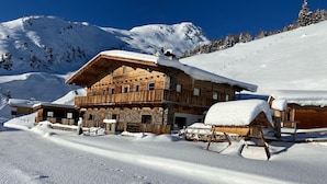 Una baita di legno con fondamenta in pietra, circondata da montagne innevate.