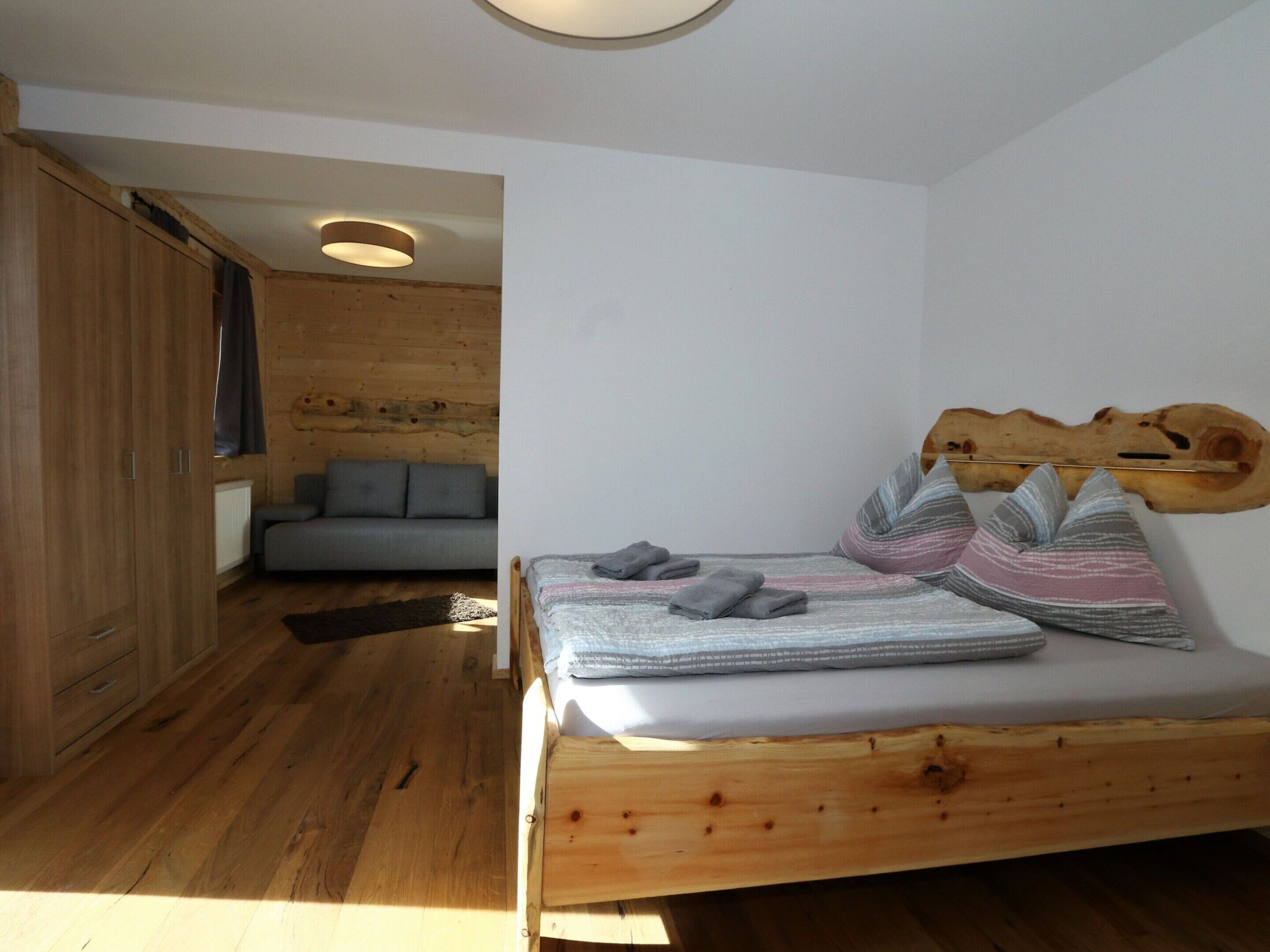 A small, cozy room with a wooden bed, a gray sofa, and a wooden wall.