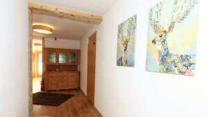 Un corridoio con pavimento in legno, un armadietto in legno con ante in vetro e due quadri appesi al muro.