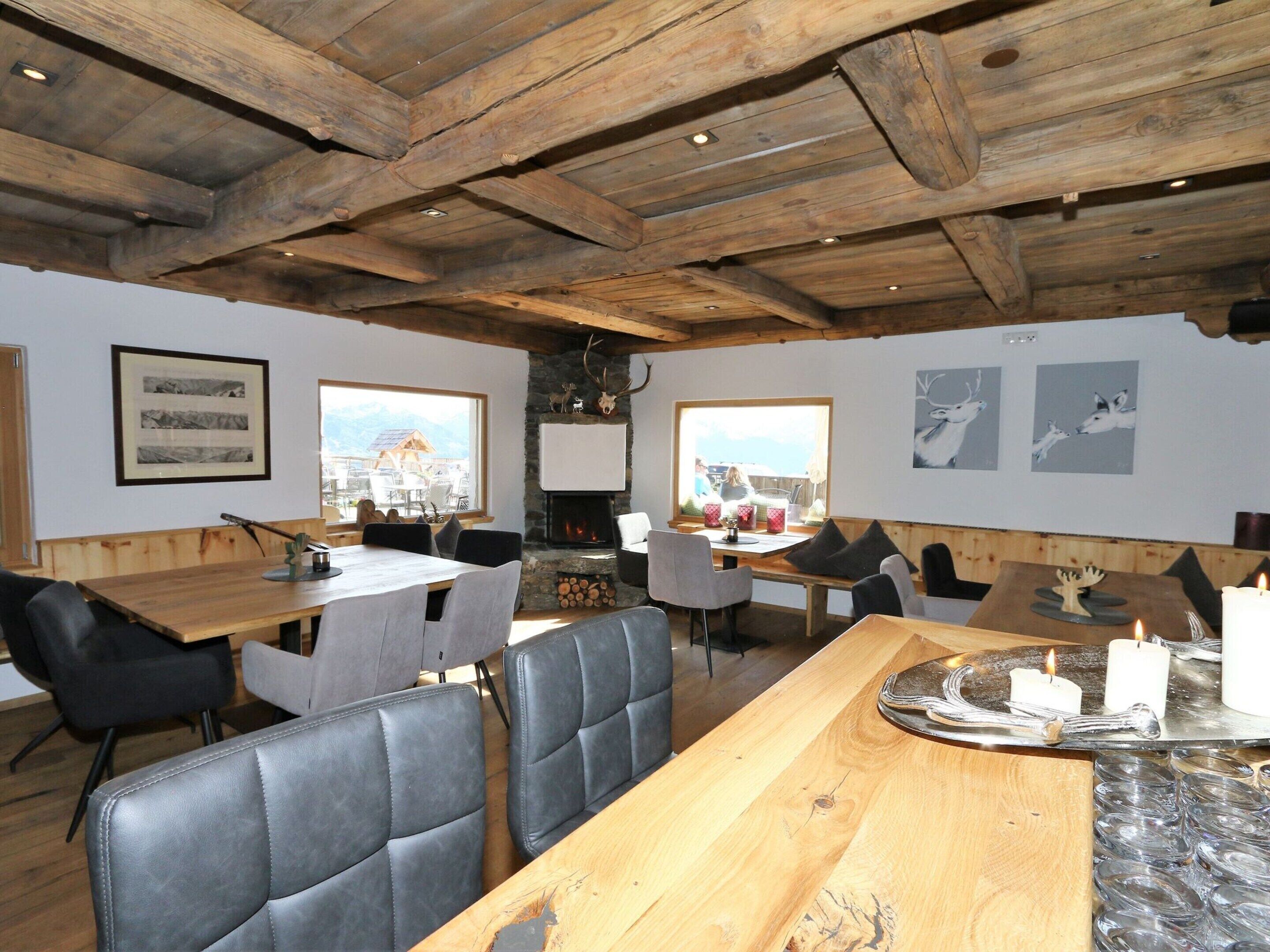 A rustic dining area with wooden tables and chairs, a fireplace, and mountain views.