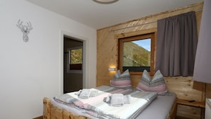 Camera da letto in una baita di legno con un letto, cuscini, una finestra e una porta.