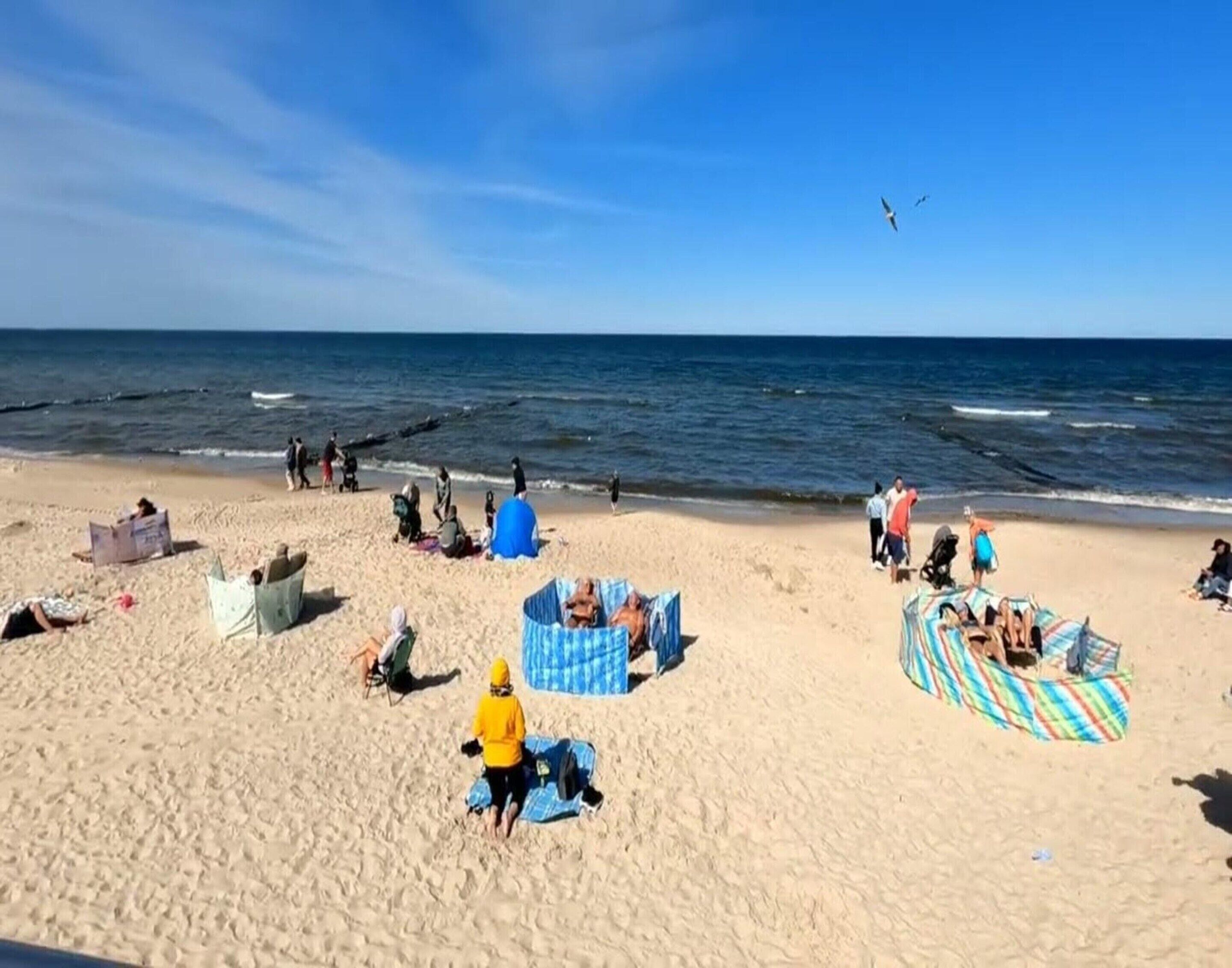 A beach with people relaxing, some in tents and others on the sand.