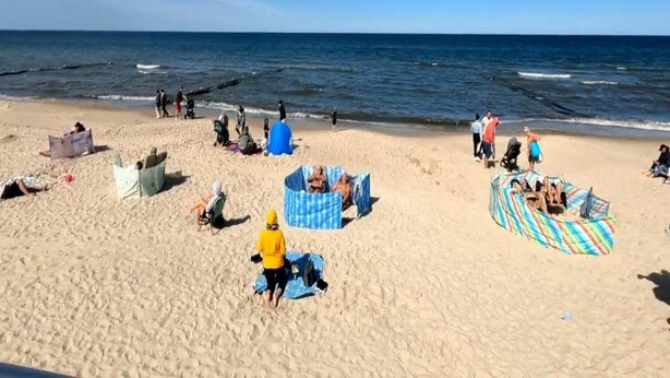 Uma praia com pessoas relaxando, algumas em barracas e outras na areia.