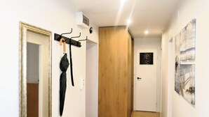 Ein Flur mit einer Holztür, einem Kleiderständer mit Regenschirmen und einem kleinen Fenster mit Blick auf Bäume.