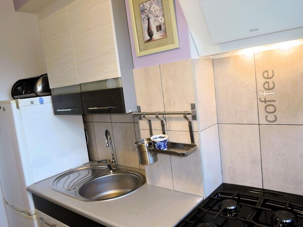 A kitchen with a stainless steel sink, a stove, and a coffee-themed wall.
